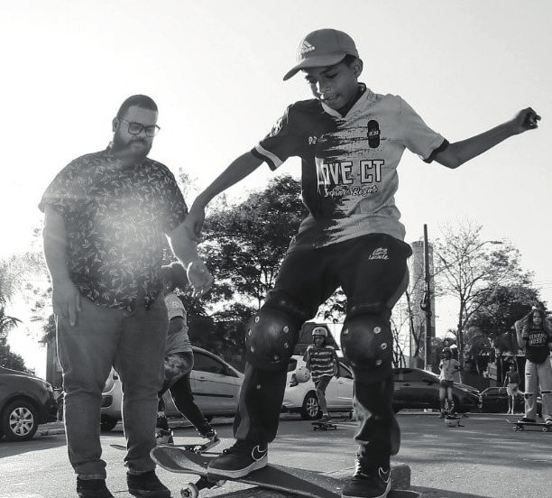 Educador ensinando criança a andar de skate, em preto e branco